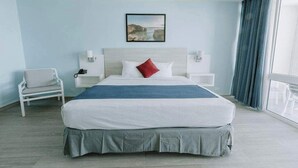 Une chambre d’hôtel avec un grand lit, une chaise, une table de chevet, une lampe fixée au mur et une fenêtre avec des rideaux.
