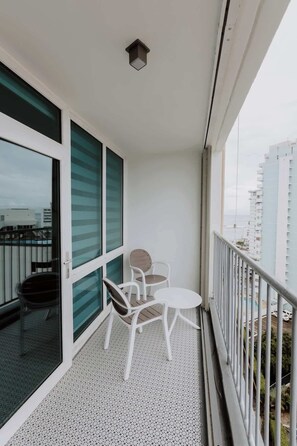 Ein Balkon mit Tisch und Stühlen, eine Glasschiebetür und Blick auf die Stadtlandschaft.