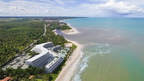 A coastal hotel with a curved building, a beach, and a view of the ocean. - Oikos Maragogi Resort - GAV Resorts (Maragogi)