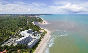 A coastal hotel with a curved building, a beach, and a view of the ocean. - Oikos Maragogi Resort - GAV Resorts (Maragogi)