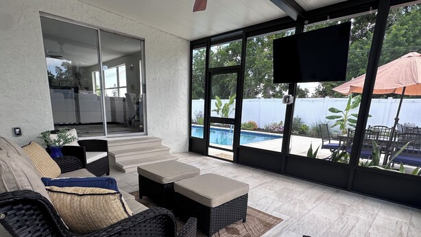 Un'area relax all'aperto coperta, con mobili in vimini, una televisione a schermo piatto e vista su una piscina.