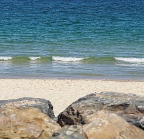 A beach with clear water, a sandy shore, and large rocks in the foreground. - *Beachfront Escape in West Beach! Ocean views, steps from the sand! (West Beach)
