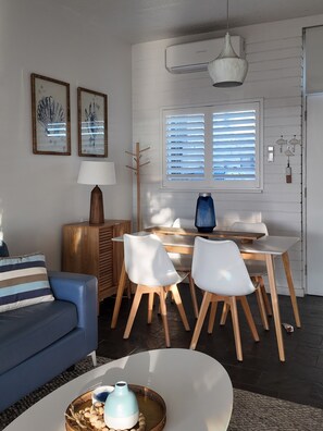 A modern living room with a sofa, dining table, chairs, a lamp, and artwork on the wall. - *Beachfront Escape in West Beach! Ocean views, steps from the sand! (West Beach)