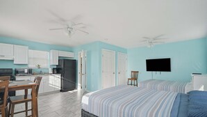 Ein Zimmer mit Bett, Fernseher, Deckenventilator und einer Küchenzeile mit Schränken und Geräten.