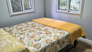 A room with a bed, two windows, and a view of greenery outside.
