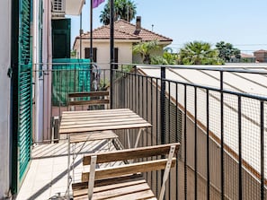 Un balcone con ringhiera in metallo, una panca in legno e un cancello verde.