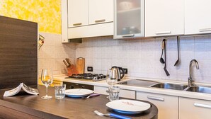 Une cuisine moderne avec des meubles blancs, une cuisinière à gaz, un évier et un plan de travail sur lequel on trouve un verre d’eau, une assiette et un livre.