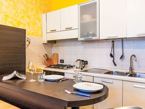 Una cucina moderna con mobili bianchi, piano cottura a gas, lavello e un piano di lavoro con un bicchiere d'acqua, un piatto e un libro.