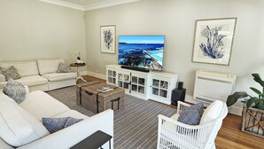 A living room with a sofa, a white baby crib, a television, and a large plant.