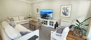 Ein Wohnzimmer mit einer Couch, einem weißen Babybett, einem Fernseher und einer großen Pflanze.