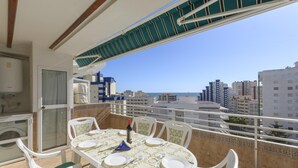 A balcony with a table set for dining, chairs, a wine bottle, and a view of the cityscape and sea. - CASA DO BRASIL - Cozy apartment with shared pool and free Wi-Fi (Gandia)