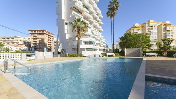 A swimming pool with a metal ladder, surrounded by palm trees and modern buildings. - CASA DO BRASIL - Cozy apartment with shared pool and free Wi-Fi (Gandia)