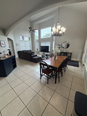 A spacious living area with a dining table, chairs, a sofa, a TV, and a ceiling fan.