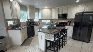 A modern kitchen with white cabinets, a central island with bar stools, a refrigerator, and a microwave. - Charming 3-bedroom house with private pool in Houston (Houston)