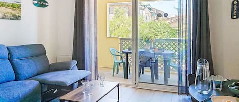 A living room with a sofa, a coffee table, a dining table with chairs, and a sliding glass door leading to an outdoor area.