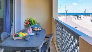 Ein Balkon mit Tisch für zwei Personen, einem Blumenstrauß und Blick auf den Strand.