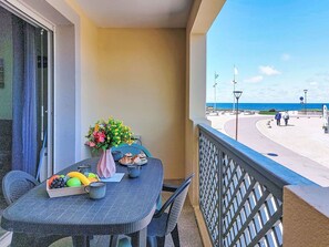 Ein Balkon mit Tisch für zwei Personen, einem Blumenstrauß und Blick auf den Strand.