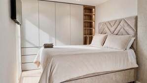 Camera da letto moderna con un letto, scaffali a muro e una TV a schermo piatto.