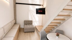 Un interno moderno con un divano, un tavolo da pranzo con sedie, una scala e una TV a muro che mostra 'NETFLIX'.