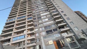 A high-rise building with multiple balconies, a gated entrance, and a sign indicating the building name.