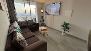 A modern living room with a sofa, a small table, a potted plant, and a TV mounted on the wall.