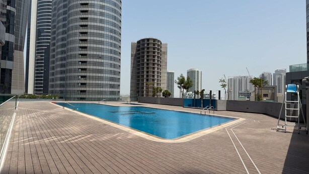 Una piscina en la azotea con plataforma de madera, rodeada de edificios altos.
