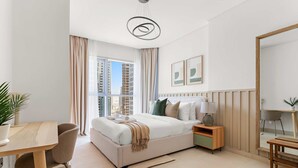 Una habitación de hotel moderna con una cama grande, un área de comedor, una mesita y un ventanal con vistas a la ciudad.