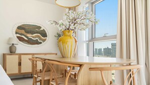 Un área de comedor moderna con una mesa redonda, sillas de madera, un jarrón amarillo con flores y una obra de arte en la pared.