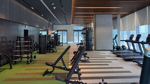 Un gimnasio con cintas de correr, máquinas de pesas y piso cubierto de moqueta verde.
