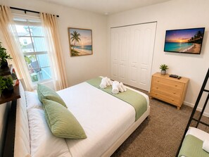 Quarto com cama, cómoda, janela com cortinas e duas imagens penduradas na parede.