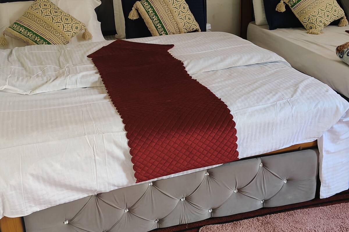Una cama con colcha blanca y roja, cabecera capitonada y almohadas estampadas.