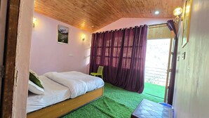 Un dormitorio con una cama, alfombra verde, una ventana con cortinas moradas y una lámpara fijada a la pared.