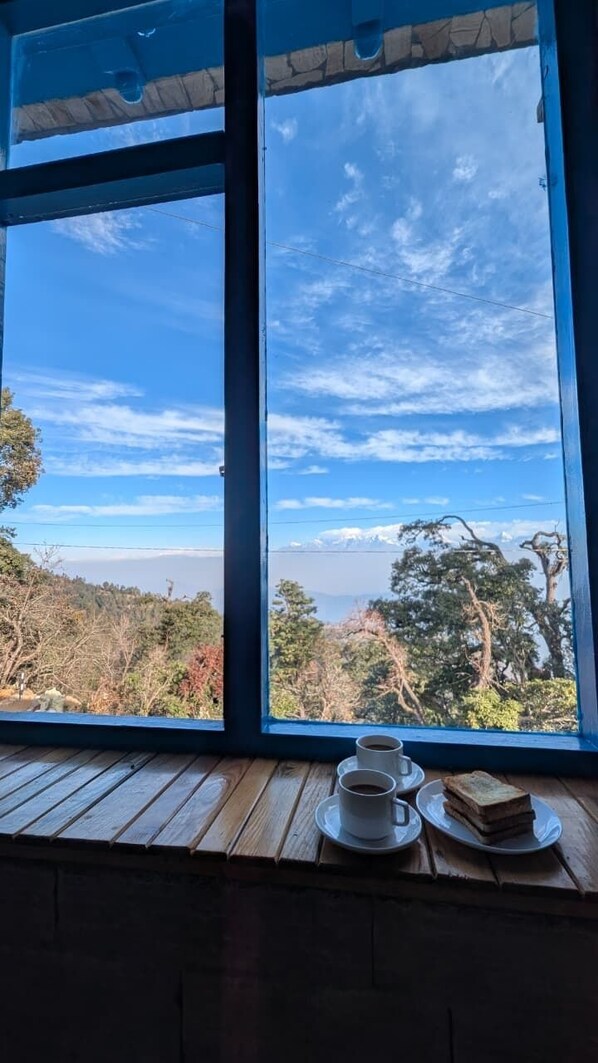 Ein Fenster mit Blick auf eine gebirgige Landschaft, ein Holztisch mit Tasse und Sandwich.