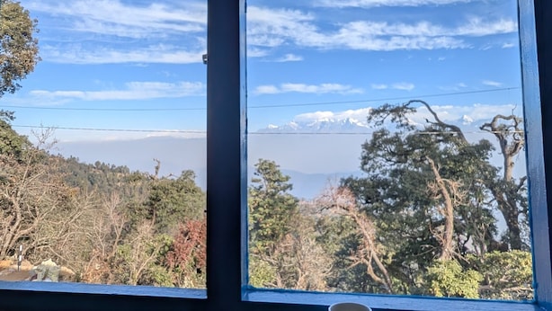 Ein Fenster mit Blick auf eine gebirgige Landschaft, ein Holztisch mit einer Kaffeetasse und einer Scheibe Toast.