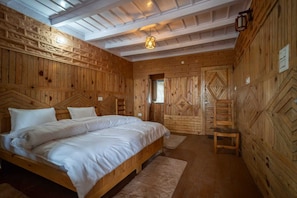 A wooden-paneled bedroom with a large bed, a small table, and a hanging light fixture.