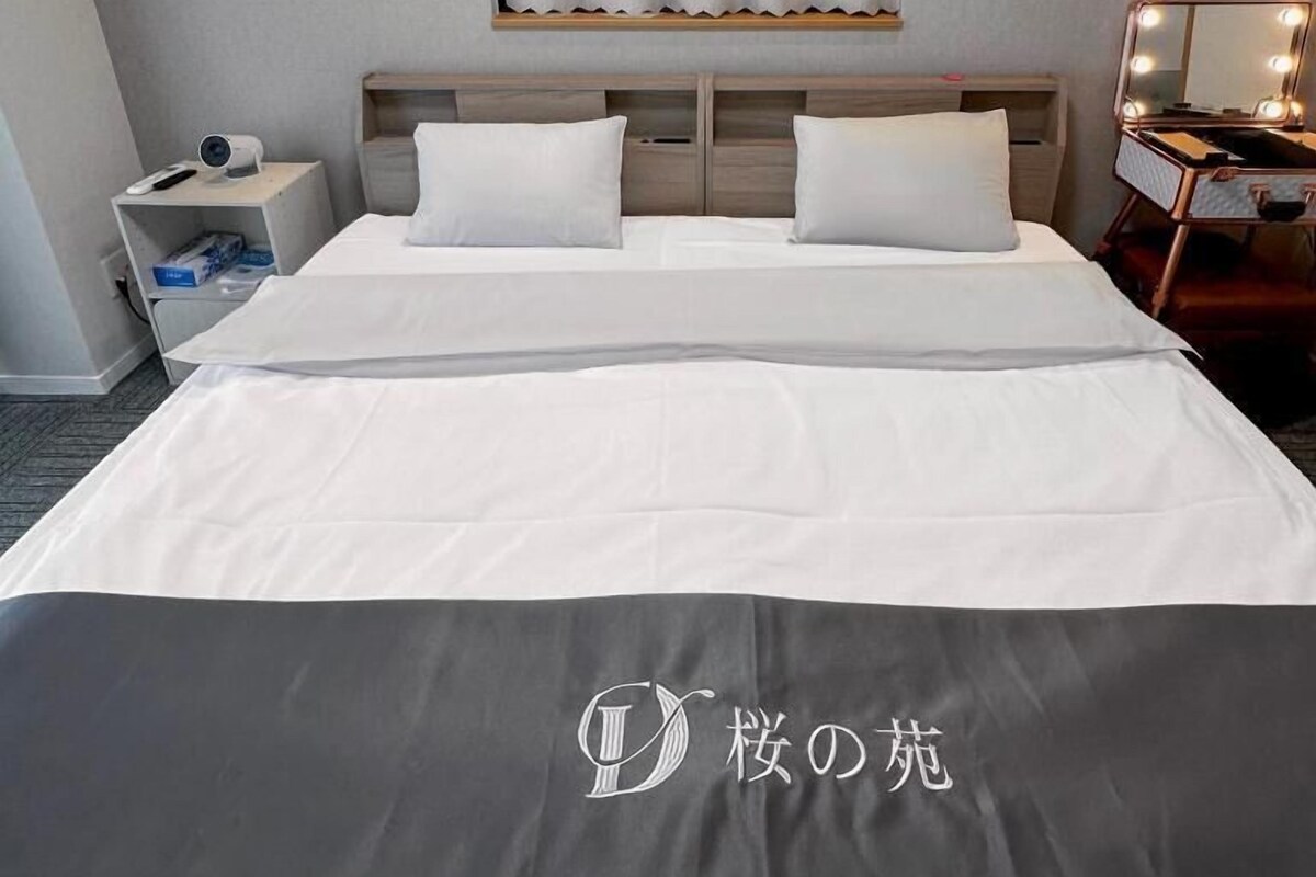 Een hotelkamer met een bed, een nachtkastje, een kaptafel met verlichting, een raam met gordijnen en een wandplank.