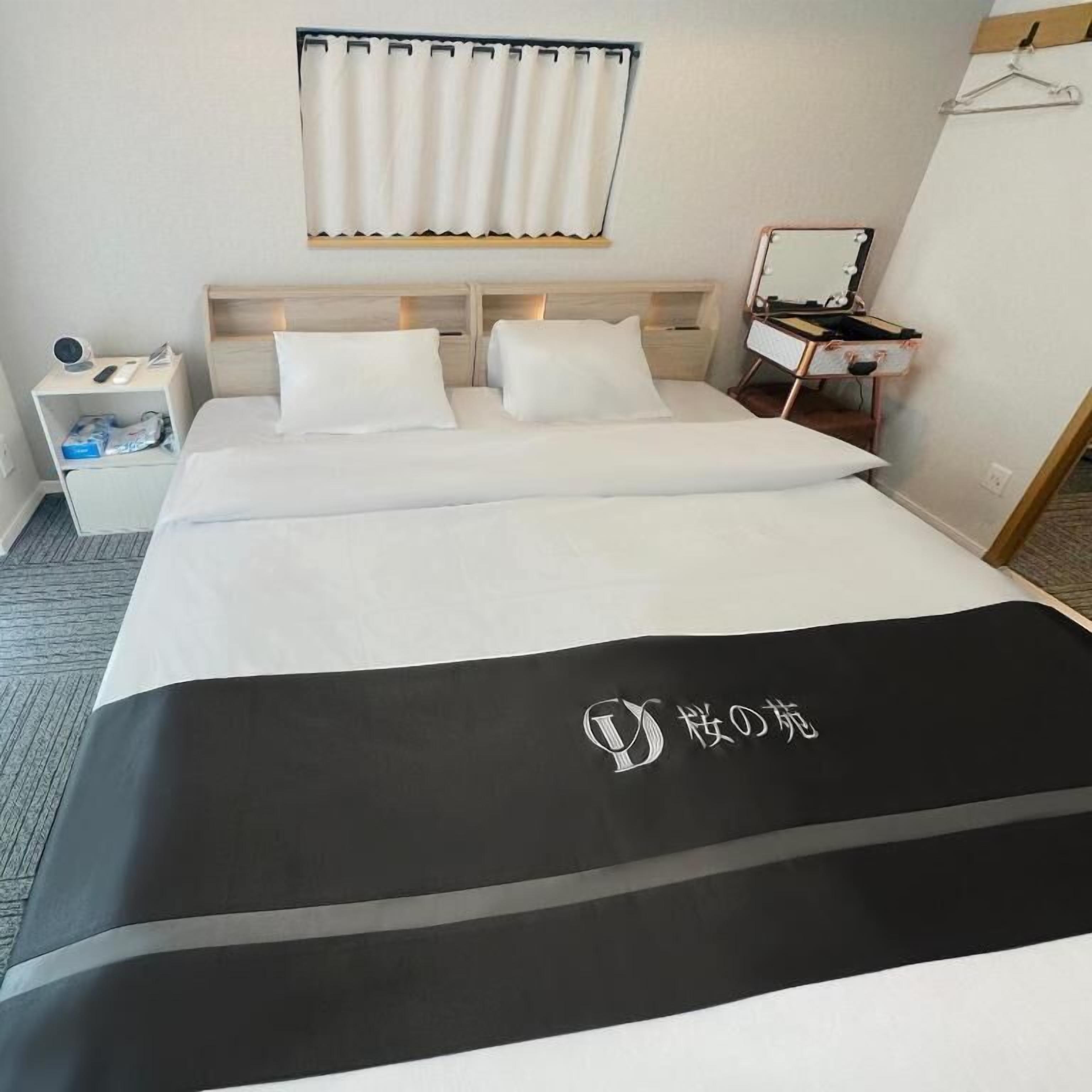 Quarto de hotel com cama, mesa de cabeceira, espelho e janela com cortinas.