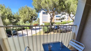 A balcony with a table and two chairs, overlooking a parking area and buildings. - 2 rooms appartement, A/C, piscine, tennis (ST MANDRIER SUR MER)