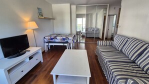A living room with a TV, a sofa, a coffee table, and a dining area with a table and chairs. - 2 rooms appartement, A/C, piscine, tennis (ST MANDRIER SUR MER)