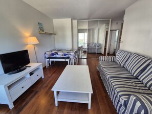 A living room with a TV, a sofa, a coffee table, and a dining area with a table and chairs. - 2 rooms appartement, A/C, piscine, tennis (ST MANDRIER SUR MER)