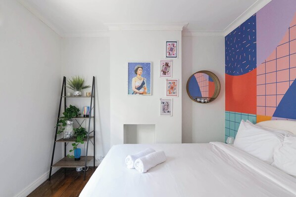 A hotel room with a bed, a shelf with plants, and a colorful wall mural.