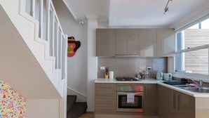 Een keuken met een fornuis, oven en spoelbak, een trap met witte leuningen en een raam met jaloezieën.