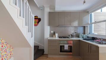 A kitchen with a stove, oven, and sink, a staircase with white railings, and a window with blinds.