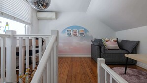 Een kamer met een houten vloer, een grijze bank, een witte balustrade en een muur met drie ingelijste foto's.