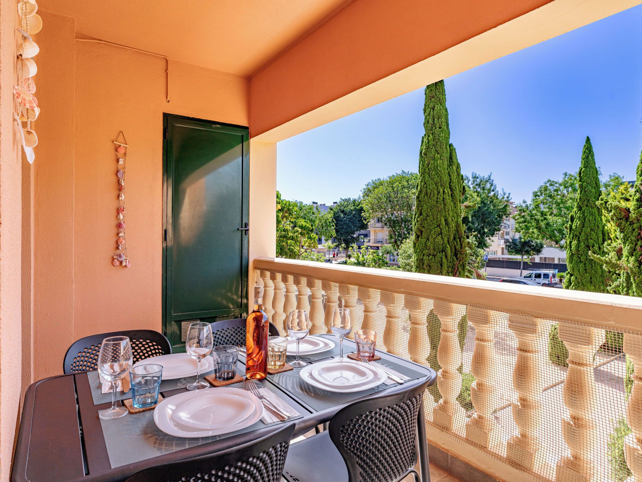 A balcony with a table set for dining, a green door, and a view of trees and buildings.
