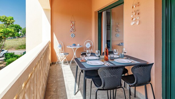 Un balcon avec une table dressée pour le repas, des chaises et une vue sur la rue.