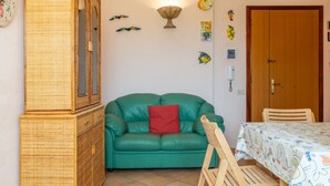 A room with a green sofa, a wooden cabinet, a dining table with a patterned tablecloth, and a wooden chair. - Bilocale la Marea - Goelba (Portoferraio)