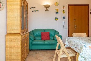 Una habitació amb un sofà verd, un armari de fusta, una taula de menjador amb una estovada estampada i una cadira de fusta.