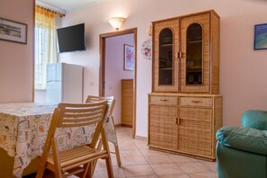 Una zona de menjador amb taula, cadires, televisió, un armari i una porta que dona a una altra habitació.
