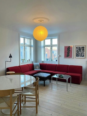 En moderne stue med en rød sofa, et rundt bord og en gul pendellampe.